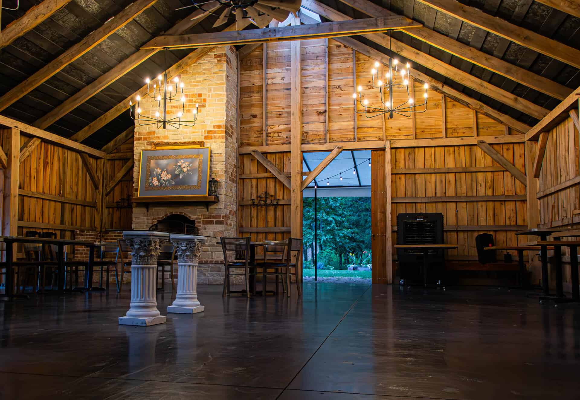 Elegant rustic barn wedding venue with exposed wood beams, brick fireplace, chandeliers, and outdoor views, ideal for weddings and events at Belle Stone Venue.
