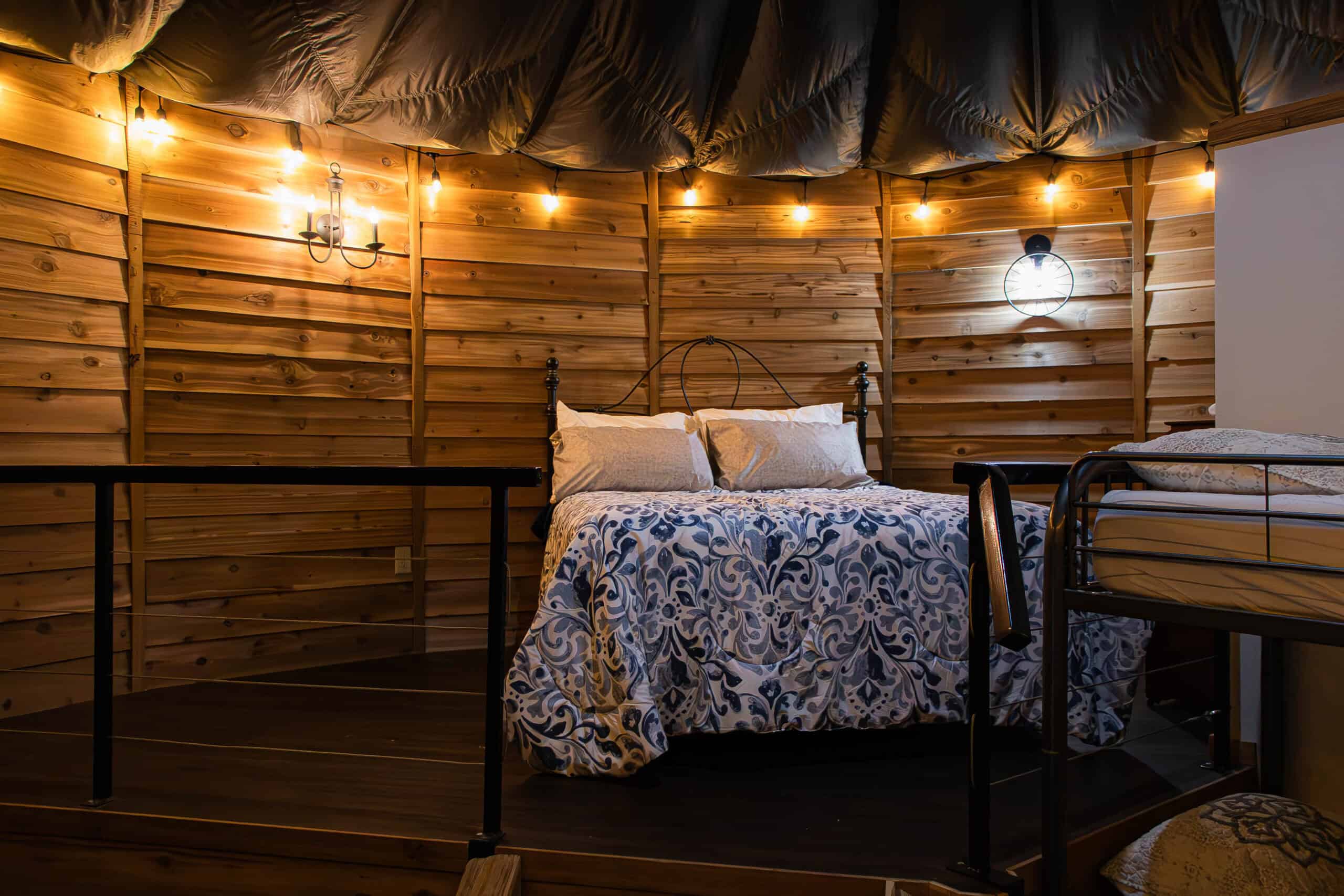 Cozy wooden interior of Belle Stone Venue with a rustic bedroom setup, warm lighting, and decorative string lights perfect for wedding accommodations or event hosting.