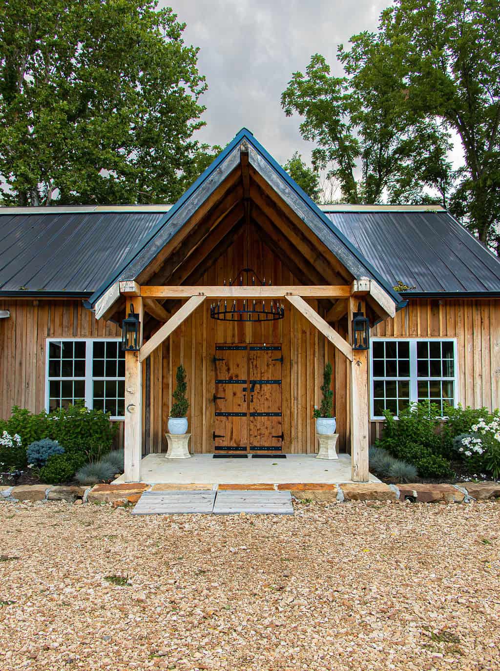 Rustic barn-style wedding venue with wooden exterior, black metal accents, and lush garden landscaping at Belle Stone Venue. Perfect setting for outdoor celebrations and events.