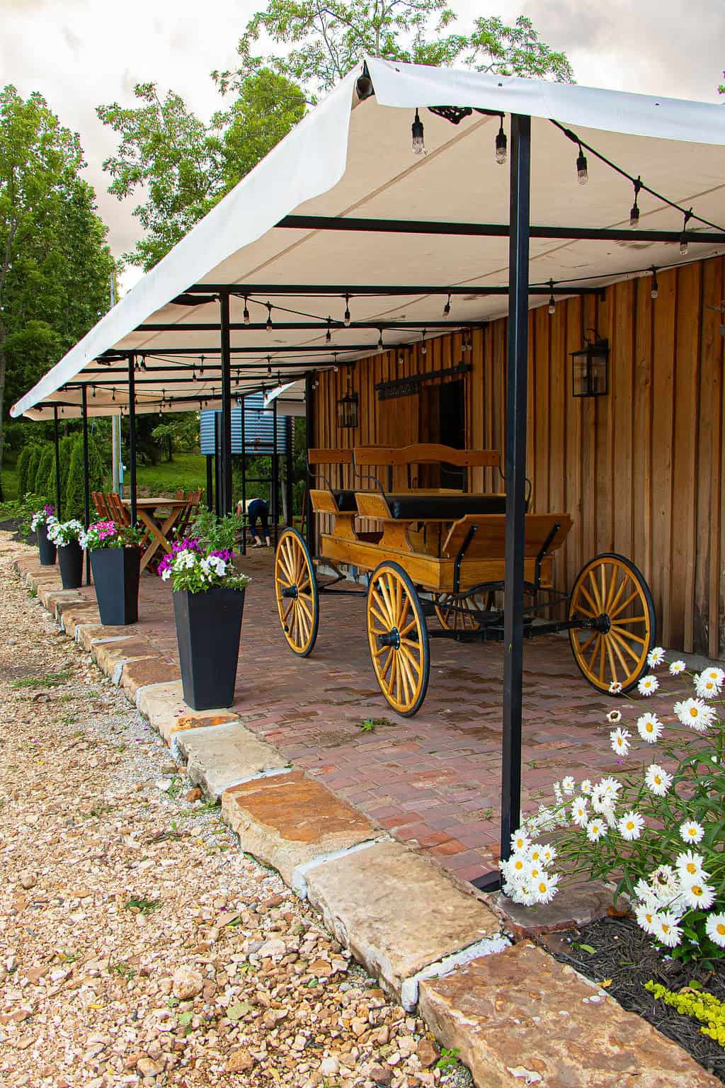 Wooden wagon and outdoor patio with string lights, flower pots, and brick walkway at Belle Stone Venue for rustic wedding and event space.