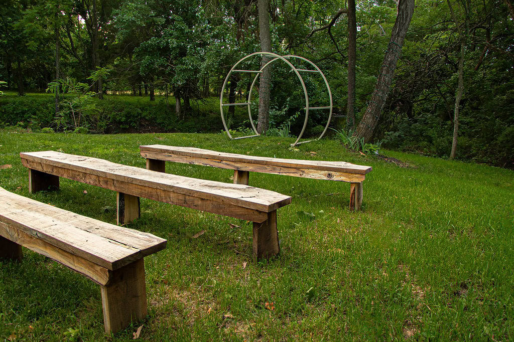 Vintage wooden benches on lush green grass in an outdoor garden setting at Belle Stone Venue.
