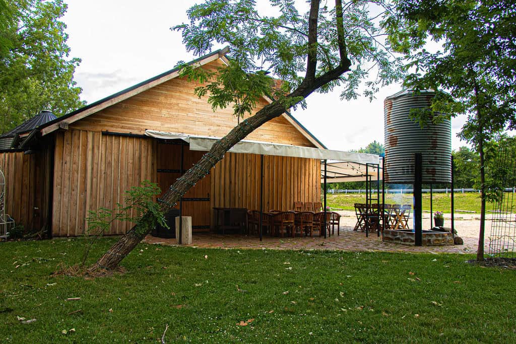 Rustic outdoor event space at Belle Stone Venue with wooden barn, seating area, water tank, and lush green surroundings for weddings and special occasions.