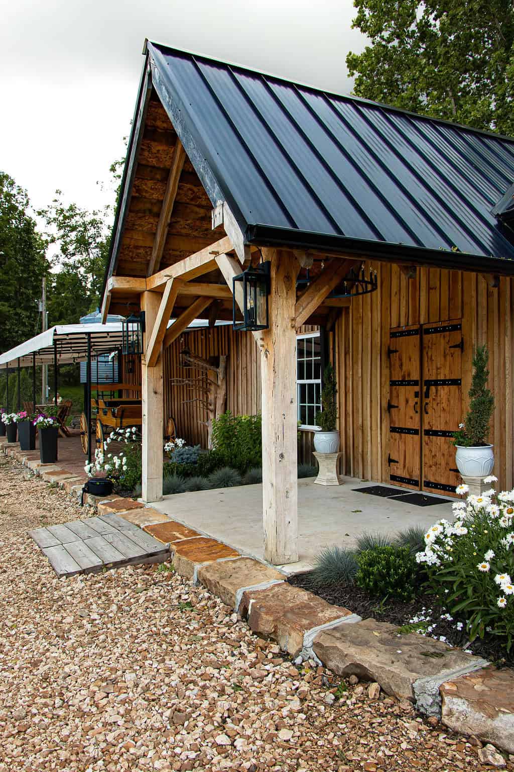 Rustic barn-style event venue with wooden exterior, black metal roof, charming flower arrangements, and outdoor seating area, perfect for weddings and outdoor celebrations at Belle Stone Venue.