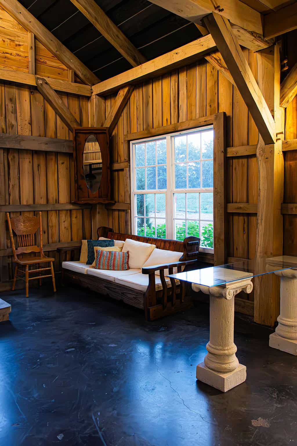 Rustic wooden barn interior with cozy seating area, vintage furniture, and large window showcasing outdoor greenery at Belle Stone Venue.