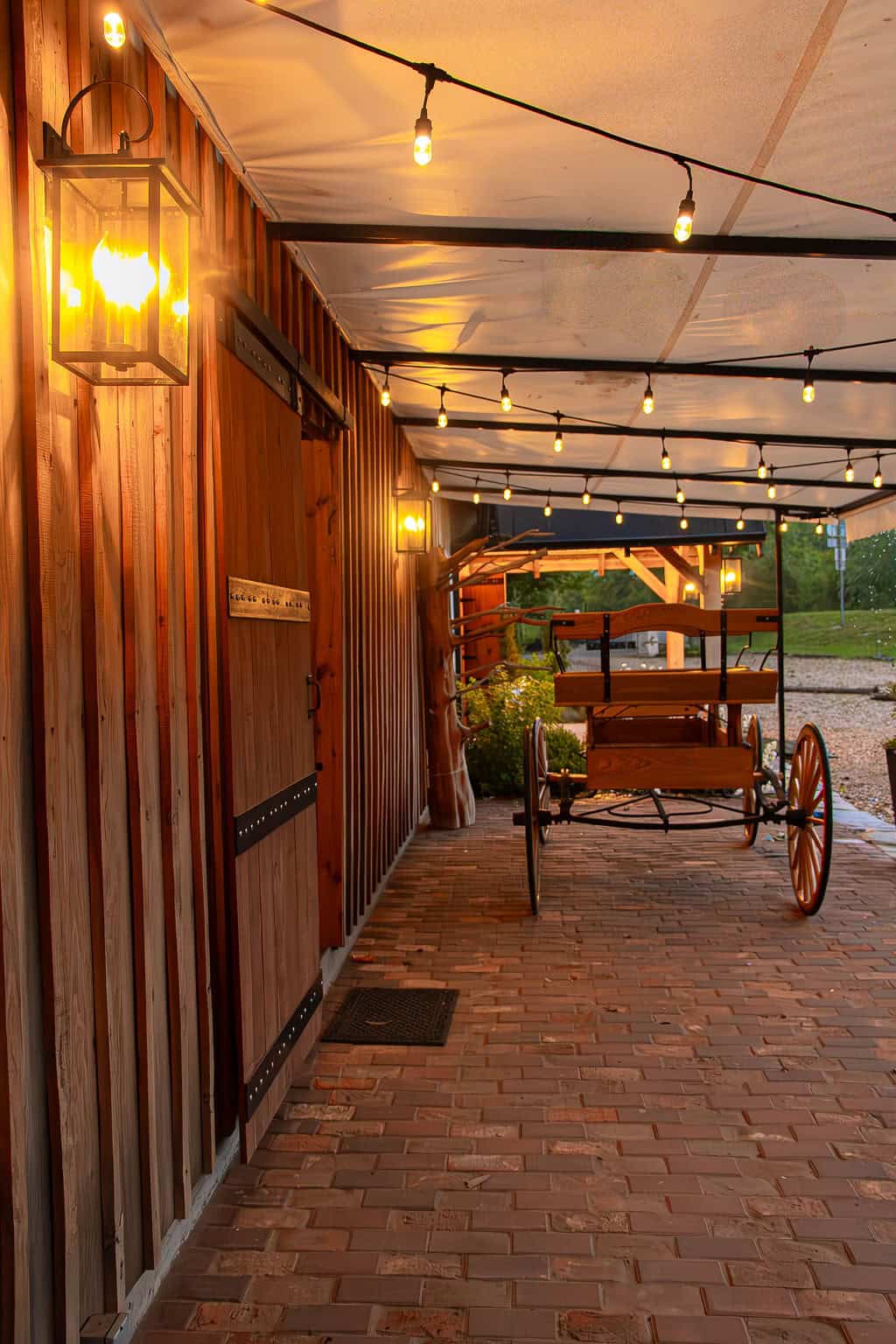 Hand-painted wooden barn with warm glowing string lights and vintage wagon decor at Belle Stone Venue for rustic outdoor wedding and event rentals in rural setting.