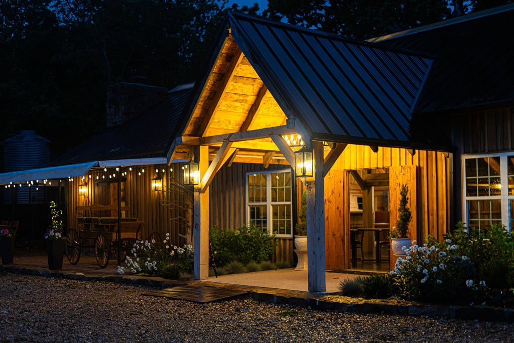 Charming rustic barn reception venue illuminated with warm lighting, surrounded by elegant flowers and outdoor decor, perfect for weddings and special events at Belle Stone Venue.