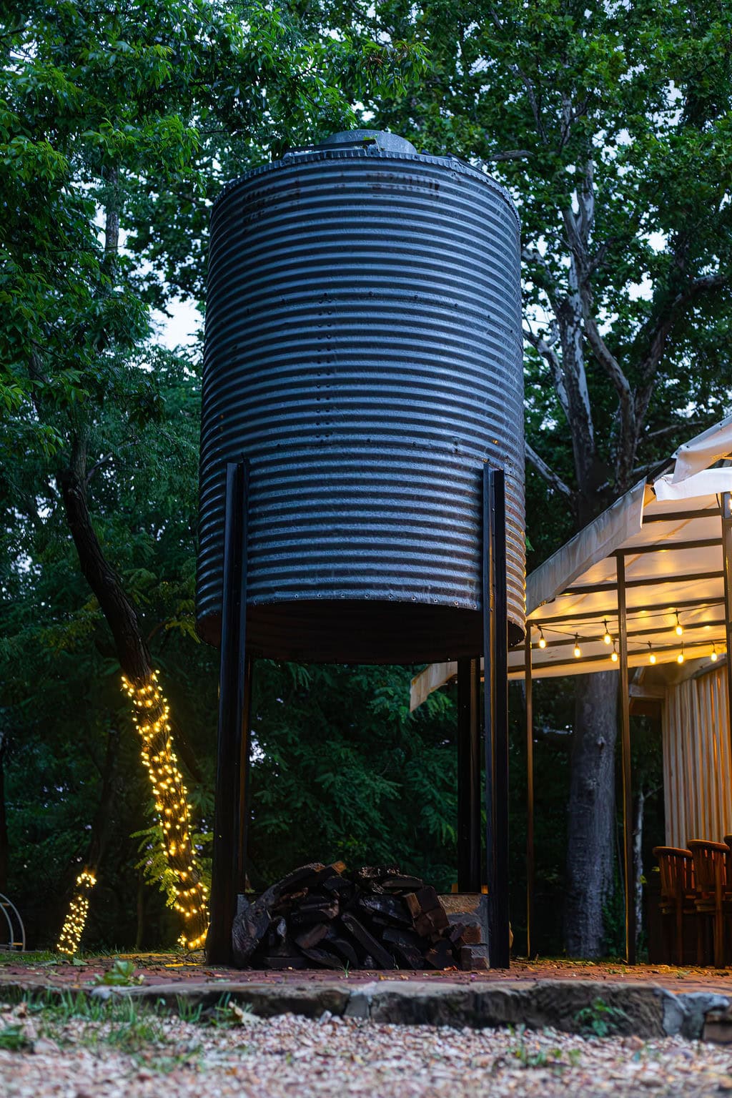 Metal water tank at Belle Stone Venue surrounded by lush trees and outdoor string lights, creating a rustic and charming ambiance for special events and outdoor celebrations.